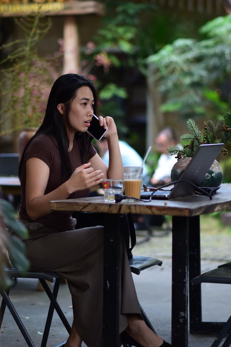 Businesswoman multitasking with a laptop and phone at an outdoor cafe.